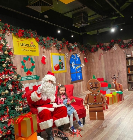 Santa seated next to Xmas tree, next to little girl and gingerbread LEGO