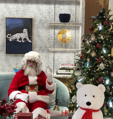 Santa Martin sitting on a light blue coach at the Cartier store in Central, Hong Kong for his Santa clause performance standing in front of a small christmas tree with a big bear next to him, the bear is from Cartier and he is performing Santa and waving for Cartier in their shop