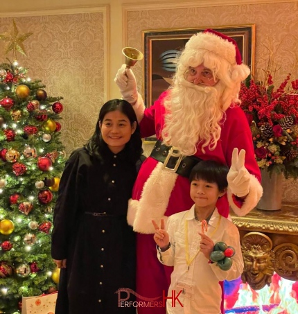 Santa Gerald standing in front of a christmas tree with 2 kids during Christmas time, at the penninsula hotel suite. Christmas tree is lit up 2025 Christmas Hong Kong
