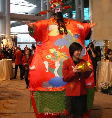 Stiltwalker in HK wearing inflatable costume taking picture with a lady holding a yuan bao at a Chinese New Year Annual dinner