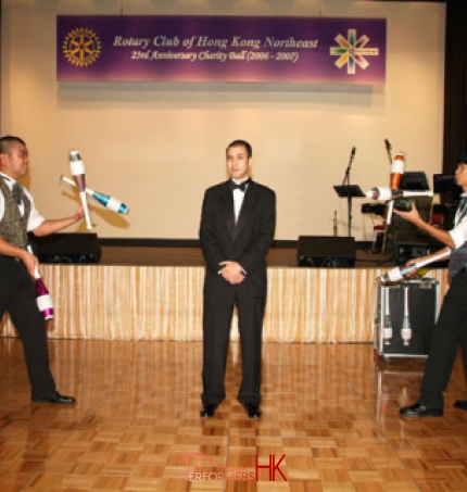Two jugglers doing a duo juggling trick, passing the cups to each other while the CEO is sting in between them at a Hong Kong corporate event
