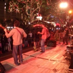 Band onstage at an outdoor event with Santa grotto in background