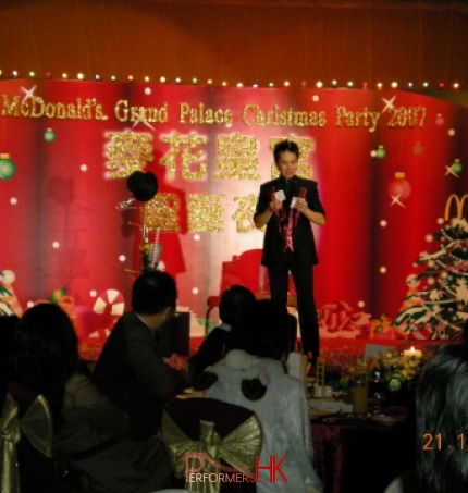 Magician standing next to the magic hat and Christmas tree performing stage card magic at Hong Kong McDonald corporate event. 